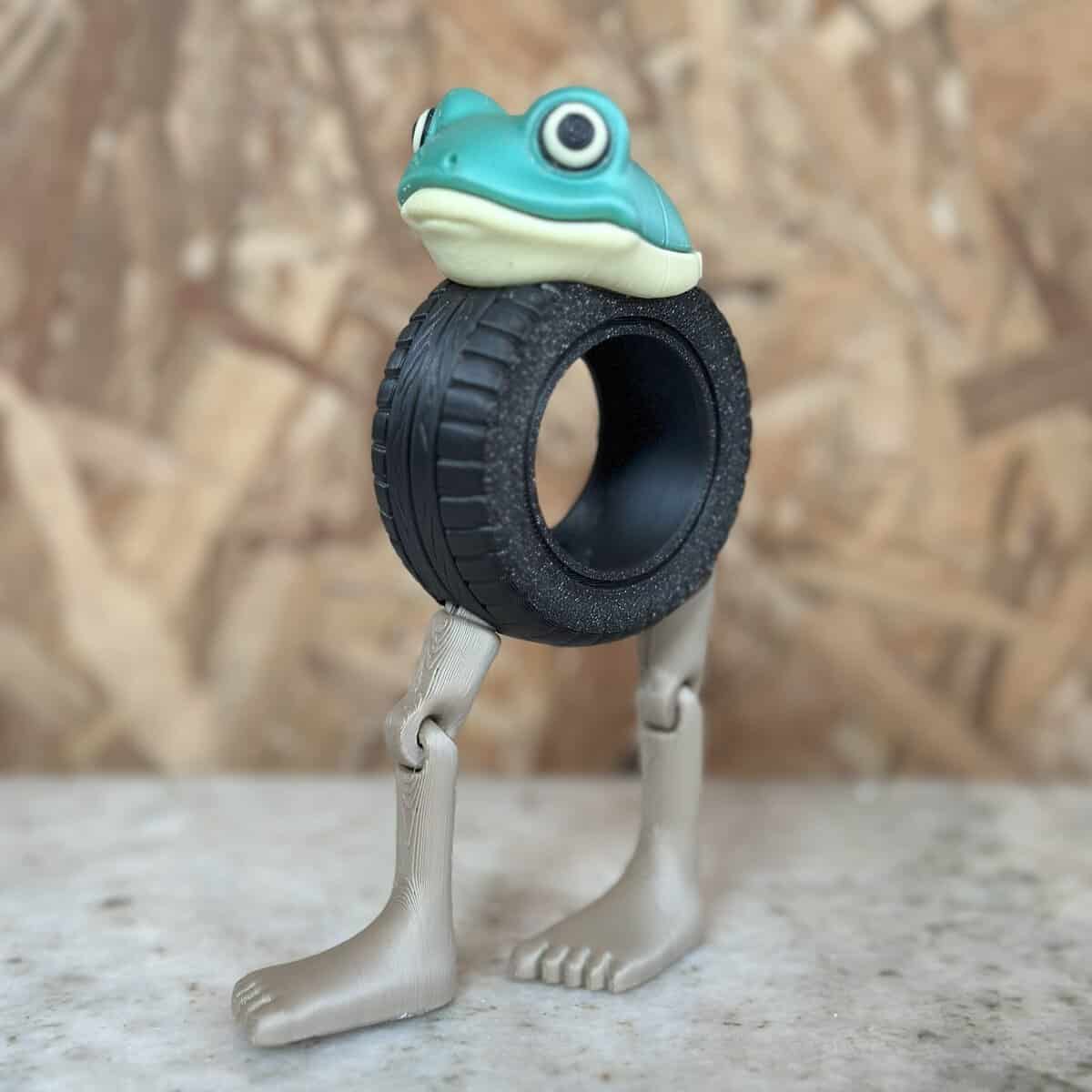 Tarrina de plástico con figura de rana y patas metálicas, utilizada como elemento decorativo o de oficina, fabricada por 3D Casa Bureu Plásticos, líder en soluciones plásticas innovadoras.