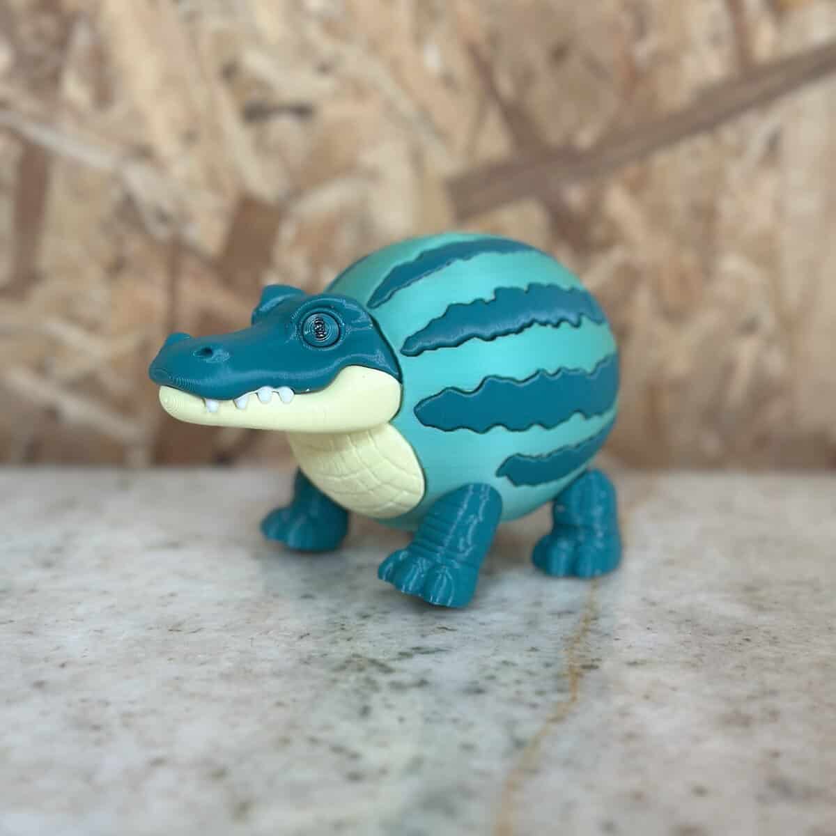 Juguete de animalitos de plástico en forma de cocodrilo, ideal para decoración o colección, fabricado por 3D Casa Bureu Plásticos, con colores llamativos y duraderos, promocionando la calidad en productos plásticos.