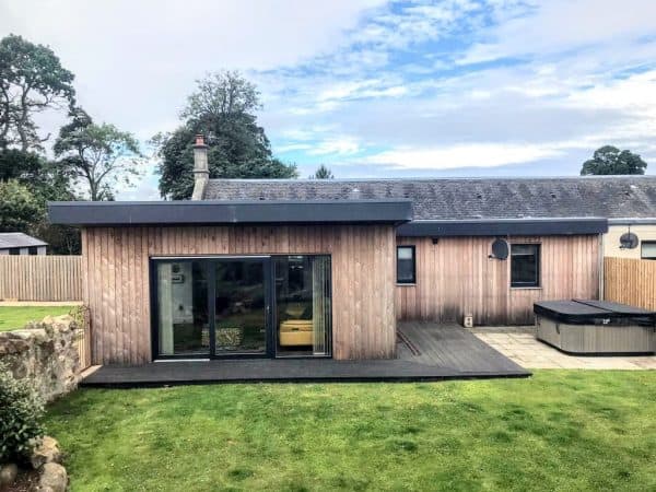 Modern wooden extension with large sliding glass doors in a private garden setting.