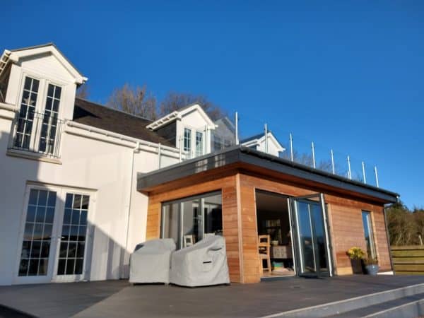 Contemporary house extension featuring wood cladding, large glass doors, and outdoor space with furniture.