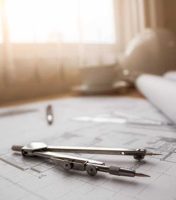Detailed architectural blueprints on desk with drawing tools.