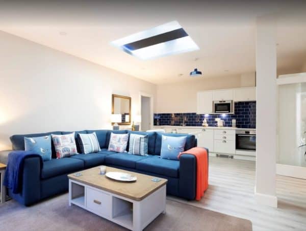 Stylish living area with a spacious blue sofa and modern kitchen, perfect for comfort and entertaining.