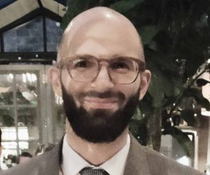 Friendly professional man in business attire, wearing glasses, in a stylish indoor setting, promoting architectural expertise.