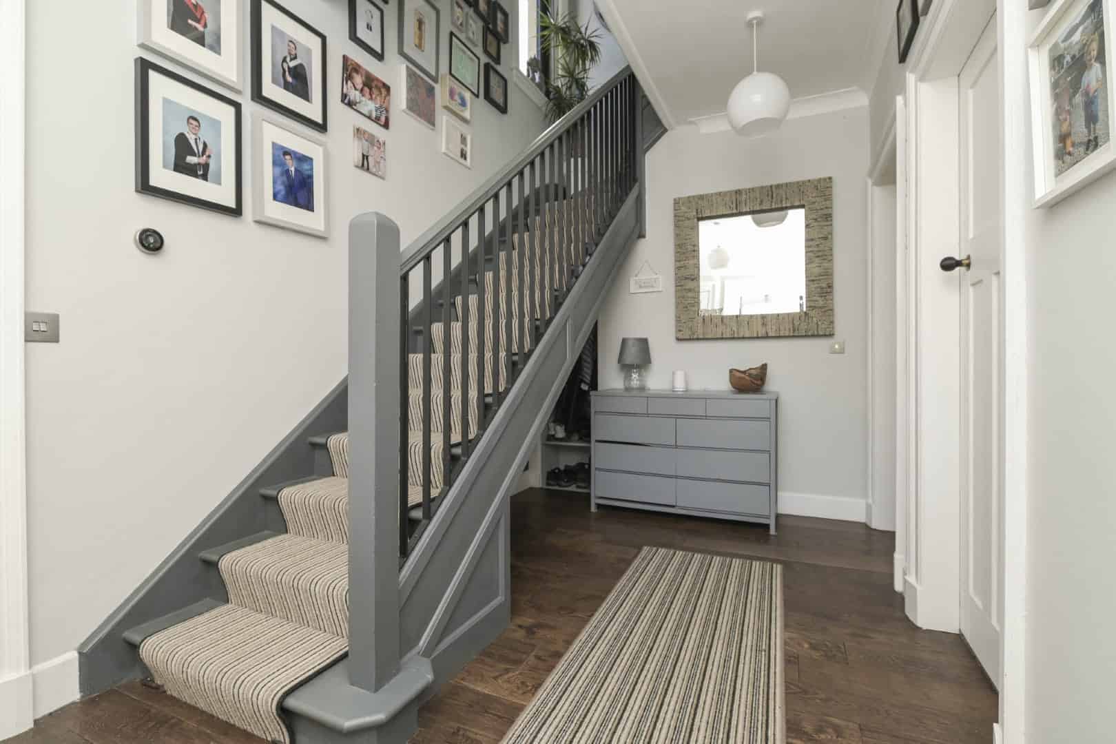 Stylish staircase with striped carpet runner leads to upper floor in contemporary home.