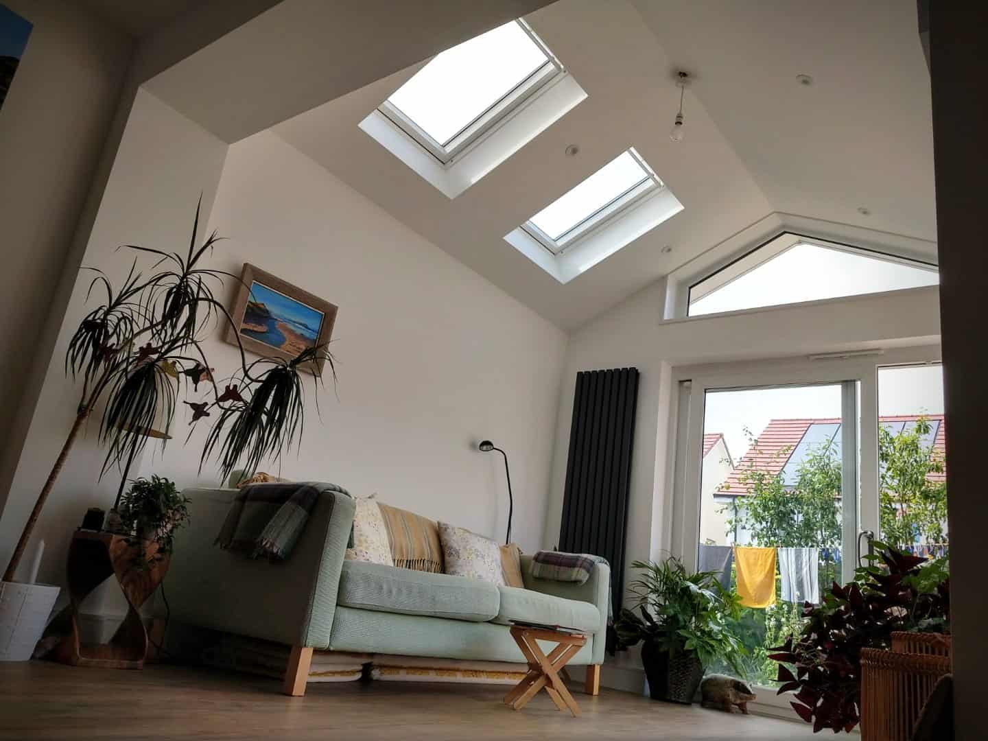 Spacious living room featuring large skylights and a big window, enhancing natural light and ventilation. Stylish plants add greenery indoors.