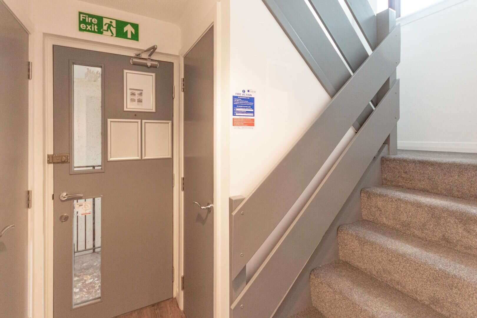 ALT text: Interior of a commercial building showing emergency exit door with fire exit sign and stairs.