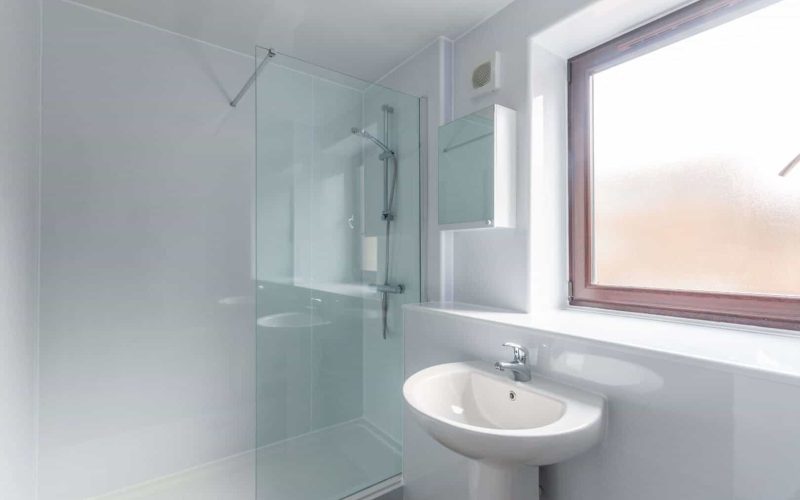 Bright, minimalist bathroom featuring a walk-in shower, white fixtures, and a large frosted window for natural lighting.