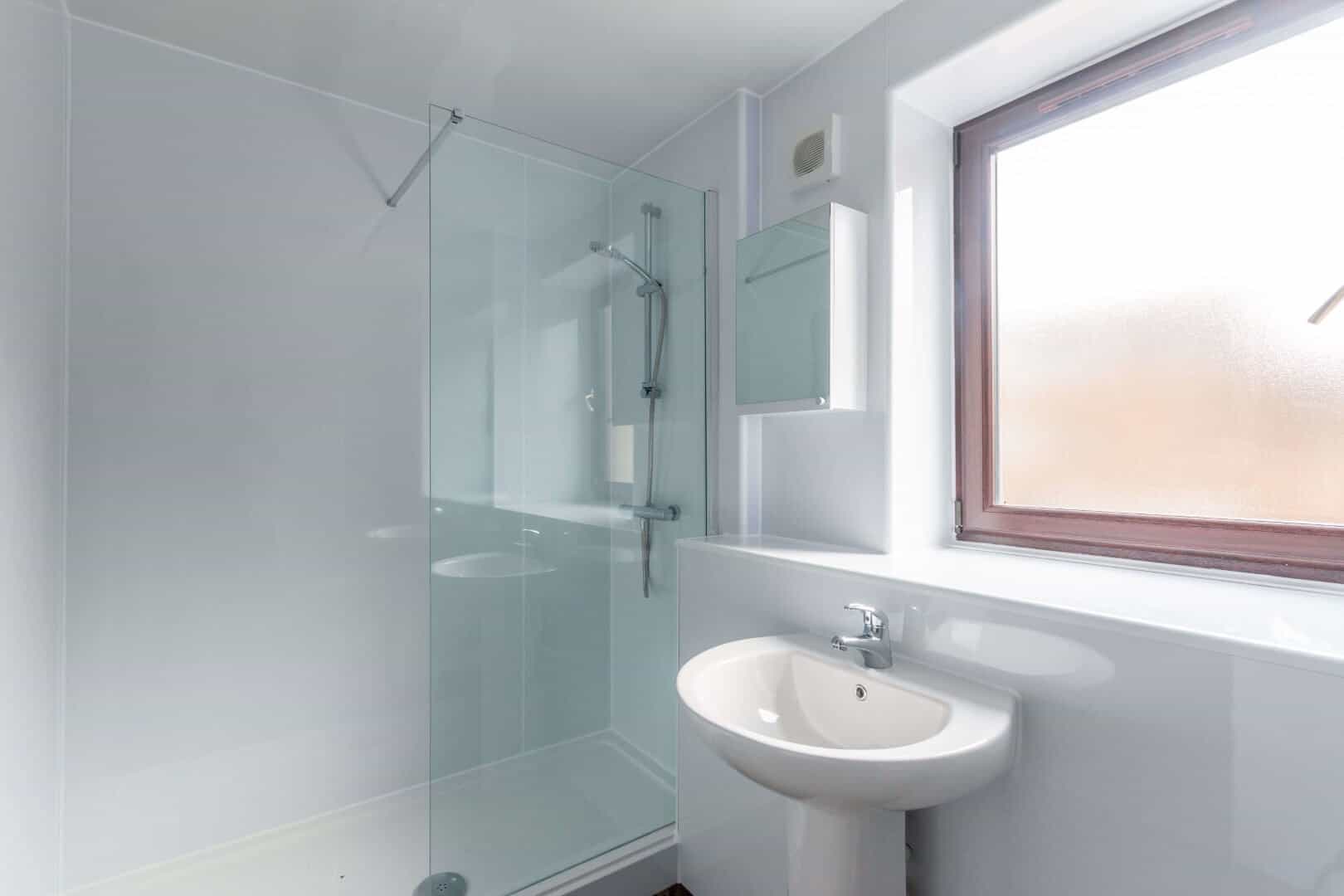 Bright, minimalist bathroom featuring a walk-in shower, white fixtures, and a large frosted window for natural lighting.
