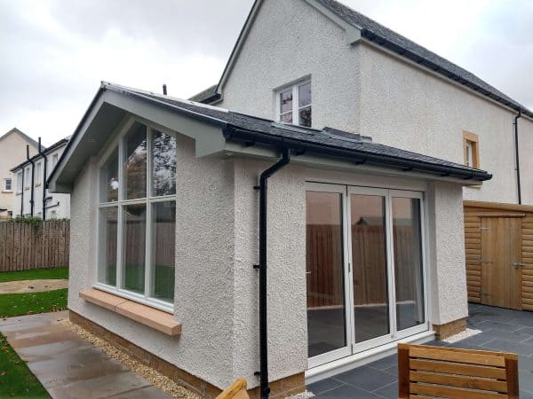 Bright home extension with large bay windows and sliding doors, blending indoor and outdoor living spaces seamlessly.