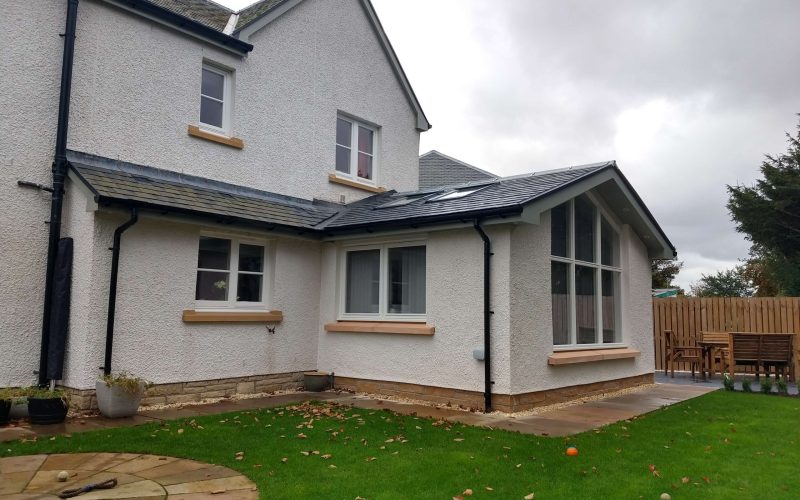 Spacious white textured house exterior with large windows and a sunny backyard, ideal for family living and outdoor entertaining.