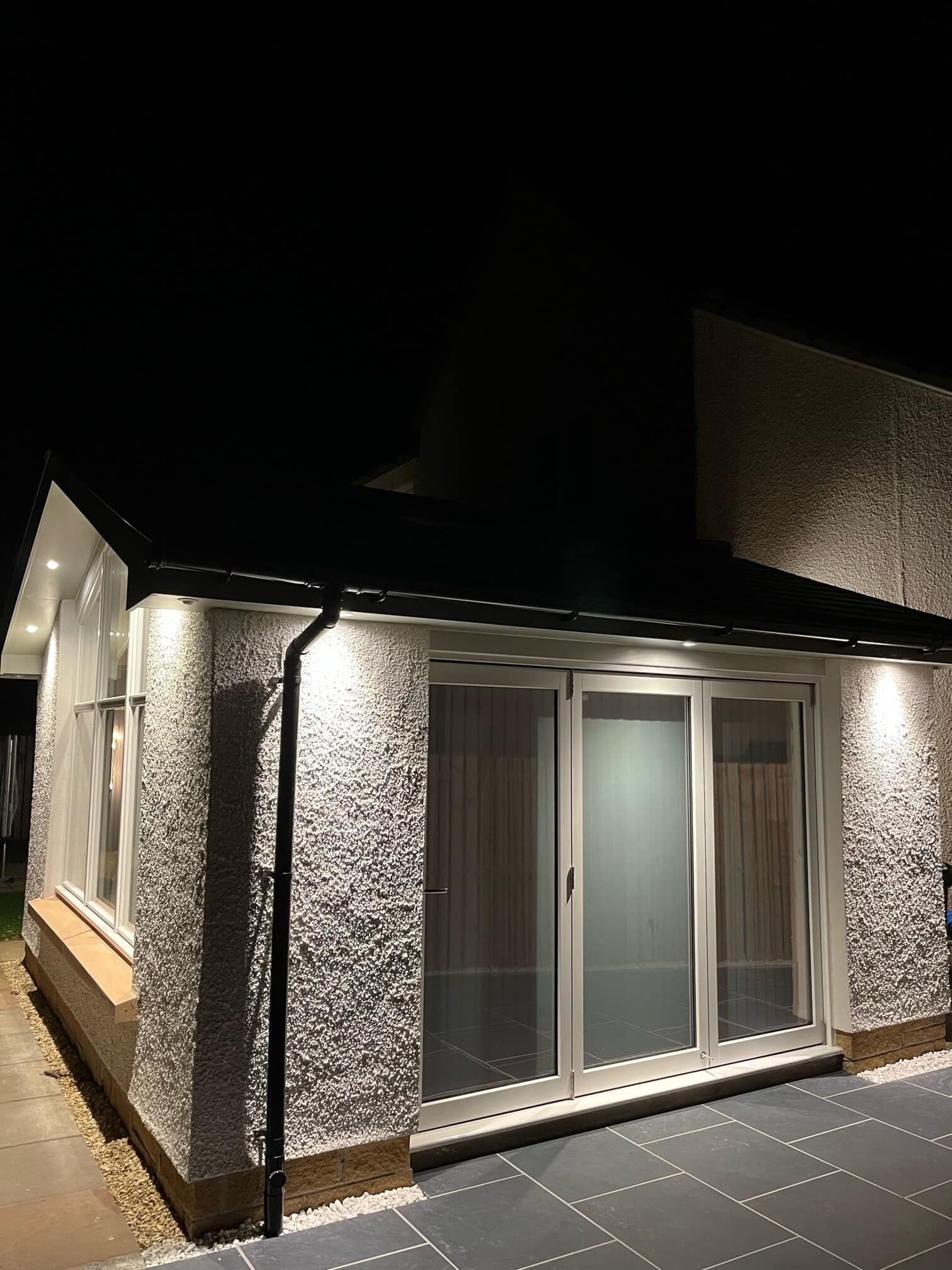 Nighttime modern house extension with sliding patio doors and outdoor lighting.