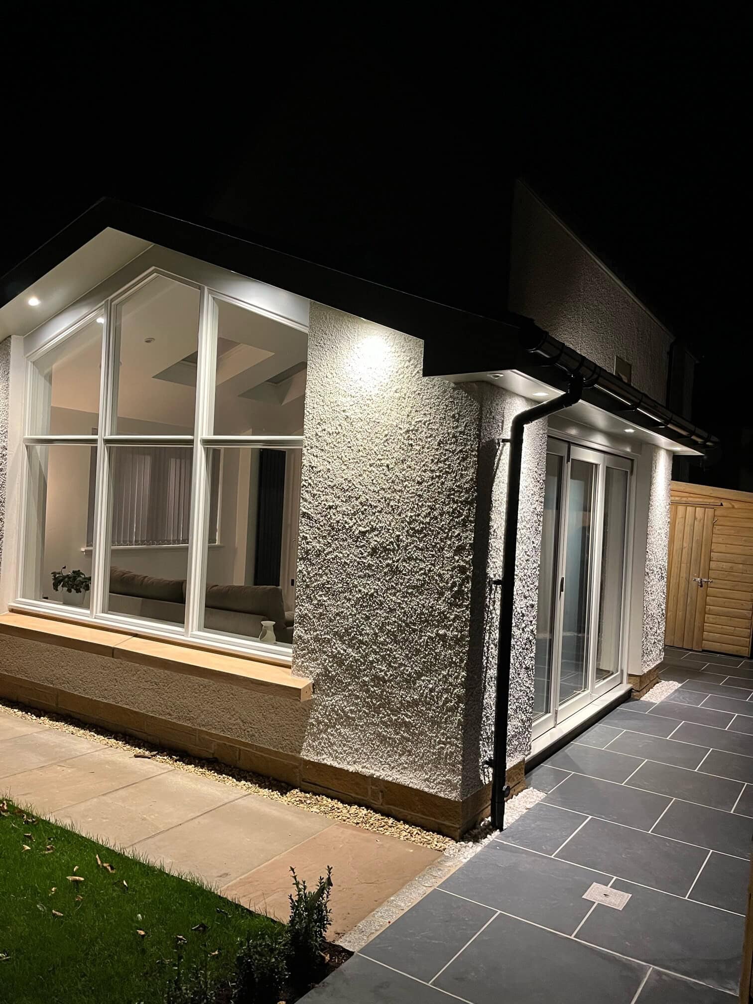Night shot of an illuminated contemporary house extension with large windows and textured white walls.