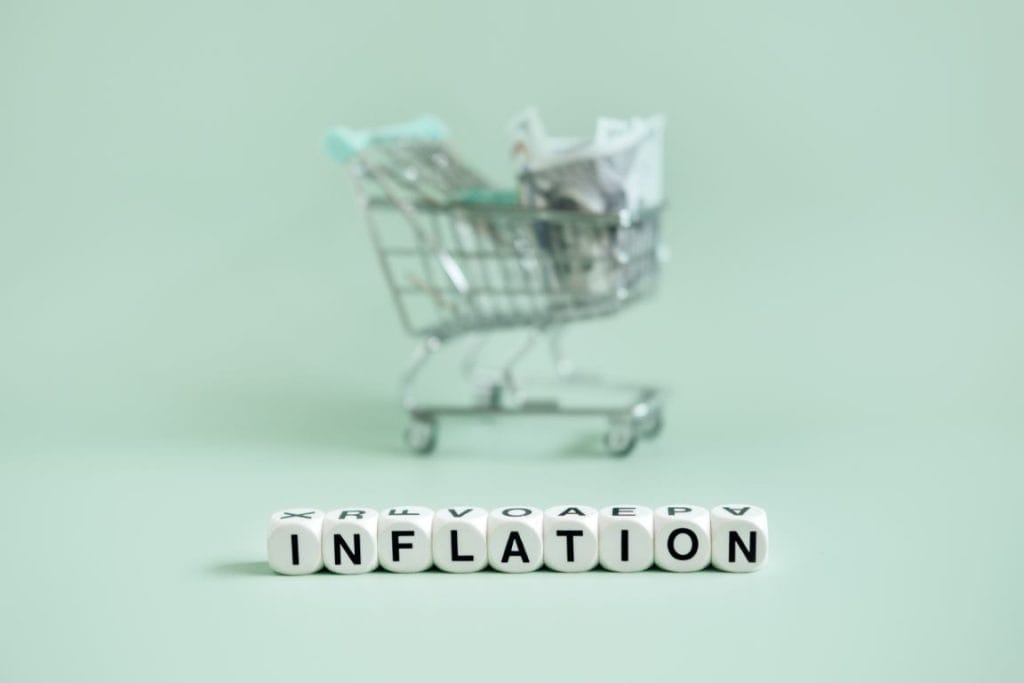 A shopping cart filled with banknotes and the word 'Inflation' spelled out in blocks, highlighting economic challenges in property development.