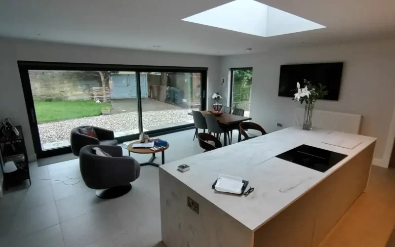 Bright, airy kitchen and dining area featuring minimalist design, marble island, large windows, and a view of the garden.
