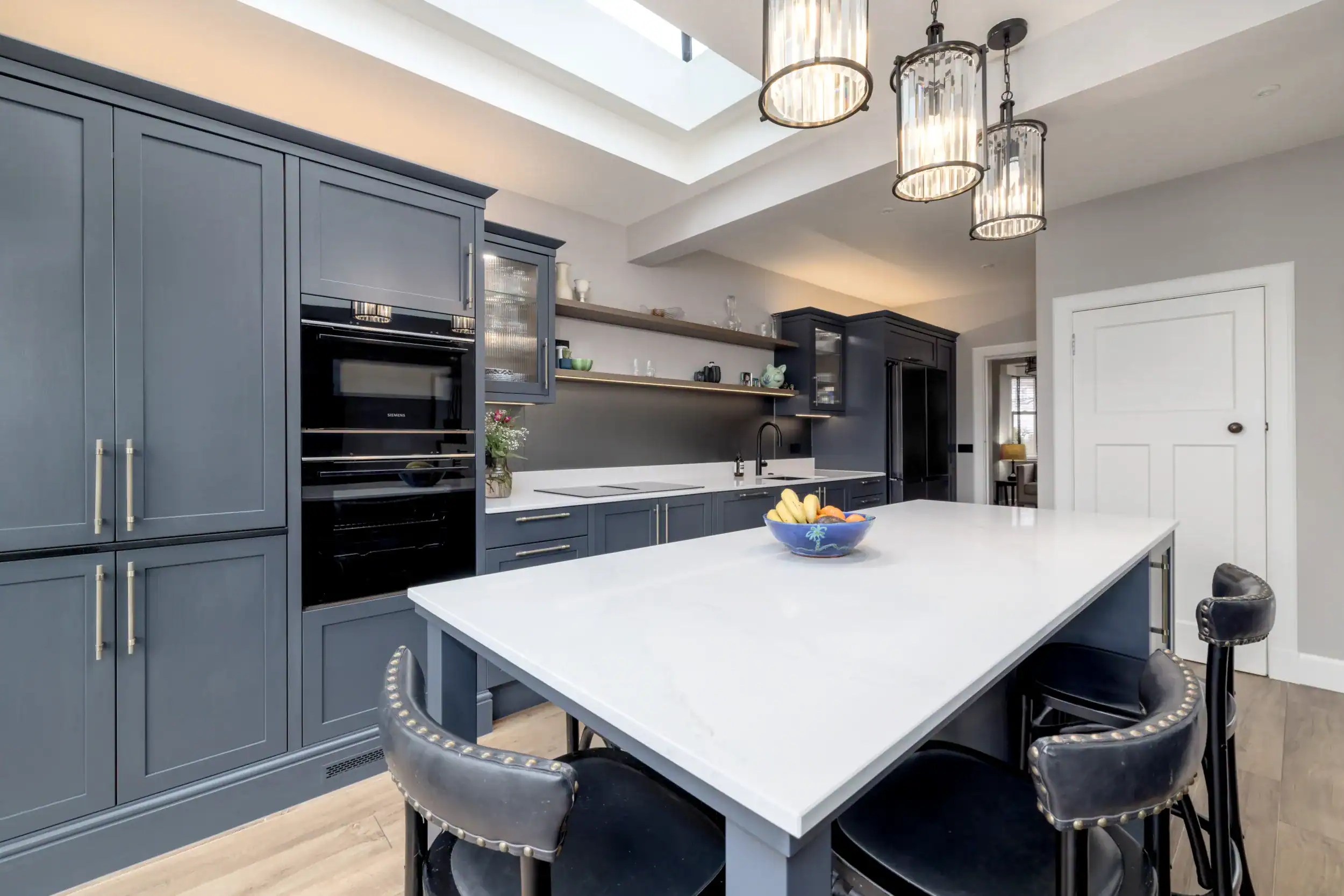 Elegant blue kitchen with white island, open shelving, and pendant lighting.