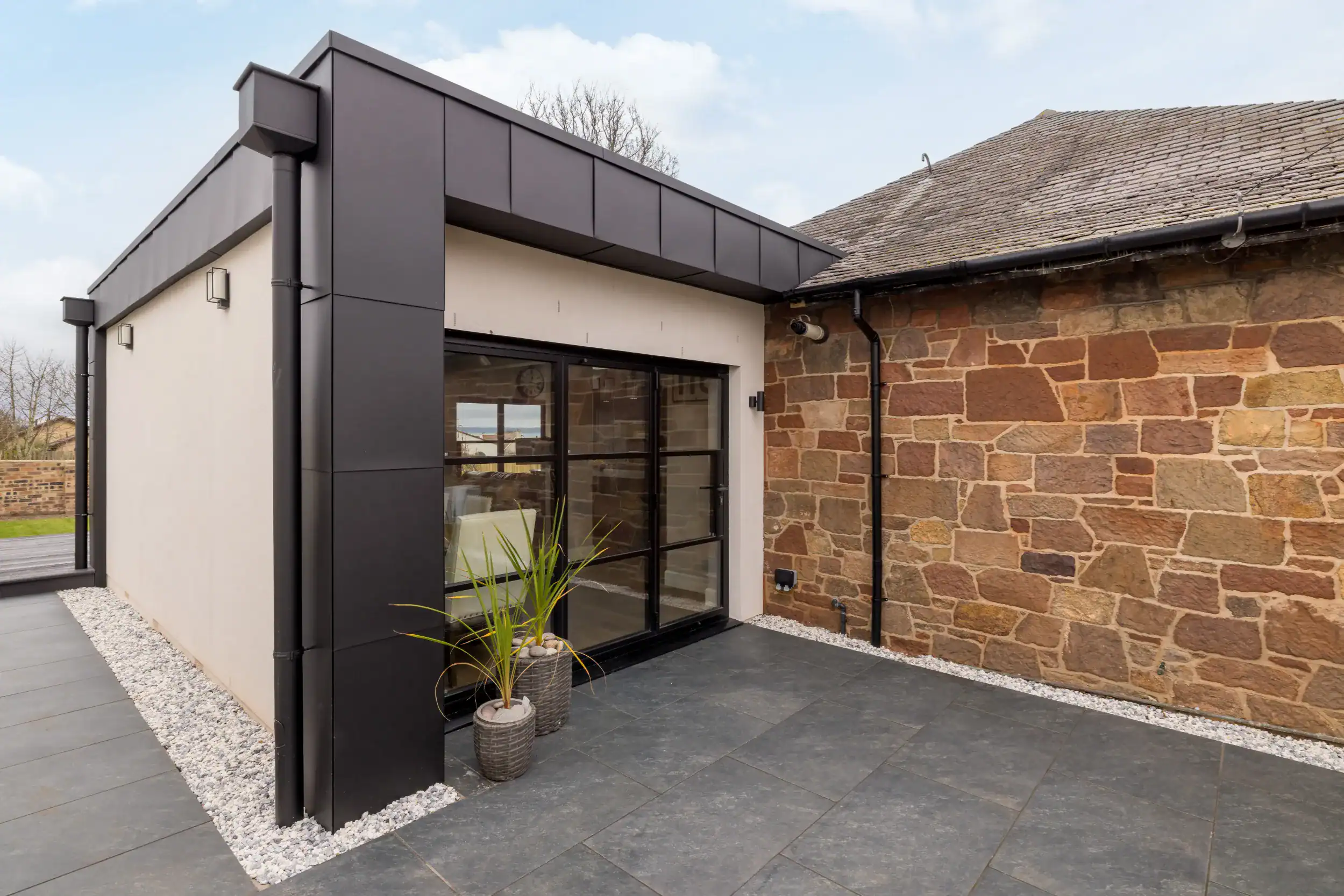 Contemporary house extension featuring black cladding and large glass doors, complementing classic brick walls.