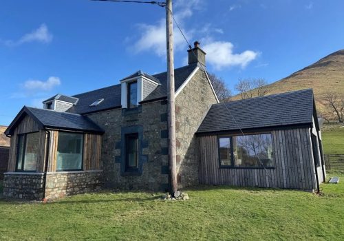 Rustic-modern residential home featuring stone walls and timber accents in a picturesque rural setting.
