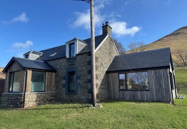 Rustic-modern residential home featuring stone walls and timber accents in a picturesque rural setting.