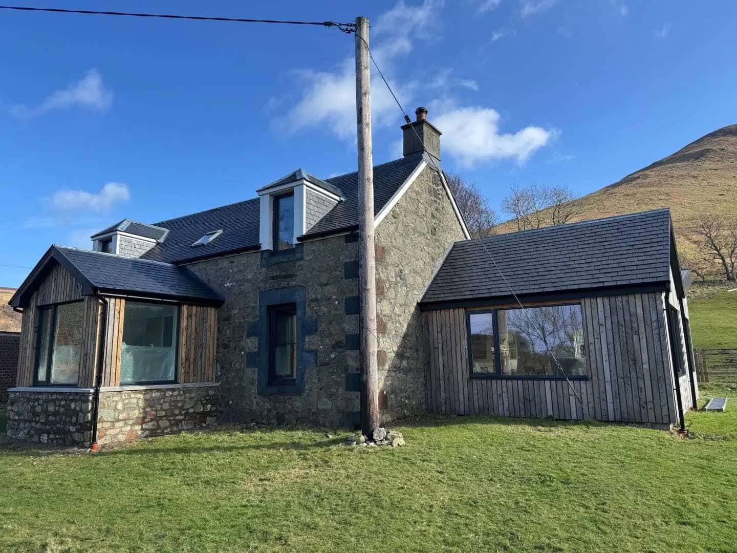 Rustic-modern residential home featuring stone walls and timber accents in a picturesque rural setting.