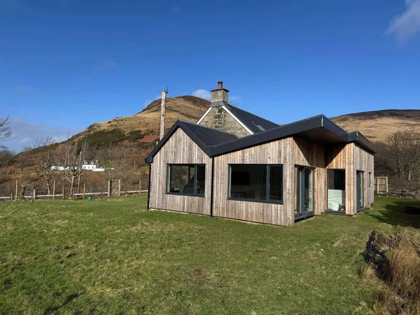 Modern eco-friendly home with timber exterior, set against hillside with blue sky and natural surroundings.