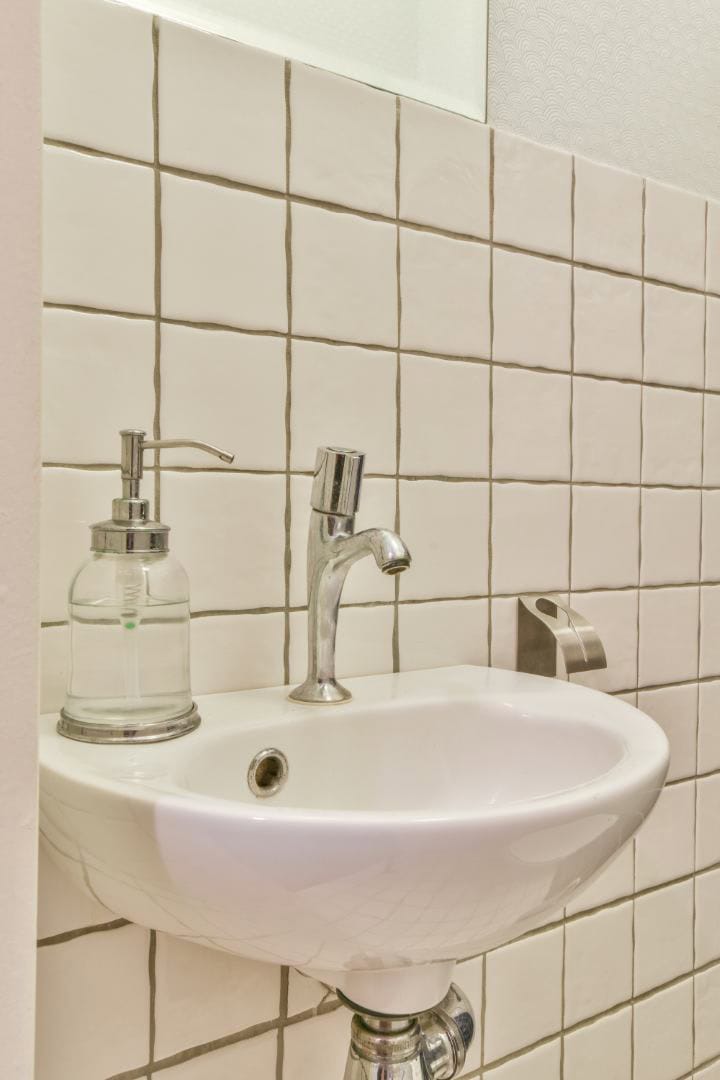 Bathroom sink with soap dispenser, stainless steel faucet, and tiled wall in modern bathroom design.