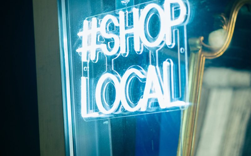 Bright neon sign reading #SHOp LOCAL on glass door.