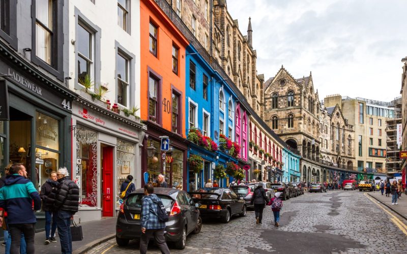 Brightly painted shop facades on a bustling city street with pedestrians and parked cars, highlighting creative architecture.