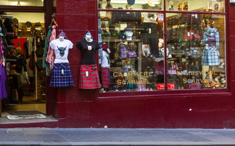 A retail storefront displaying Scottish tartan skirts, wool scarves, and accessories inside a colourful shop, celebrating Scottish heritage and style.