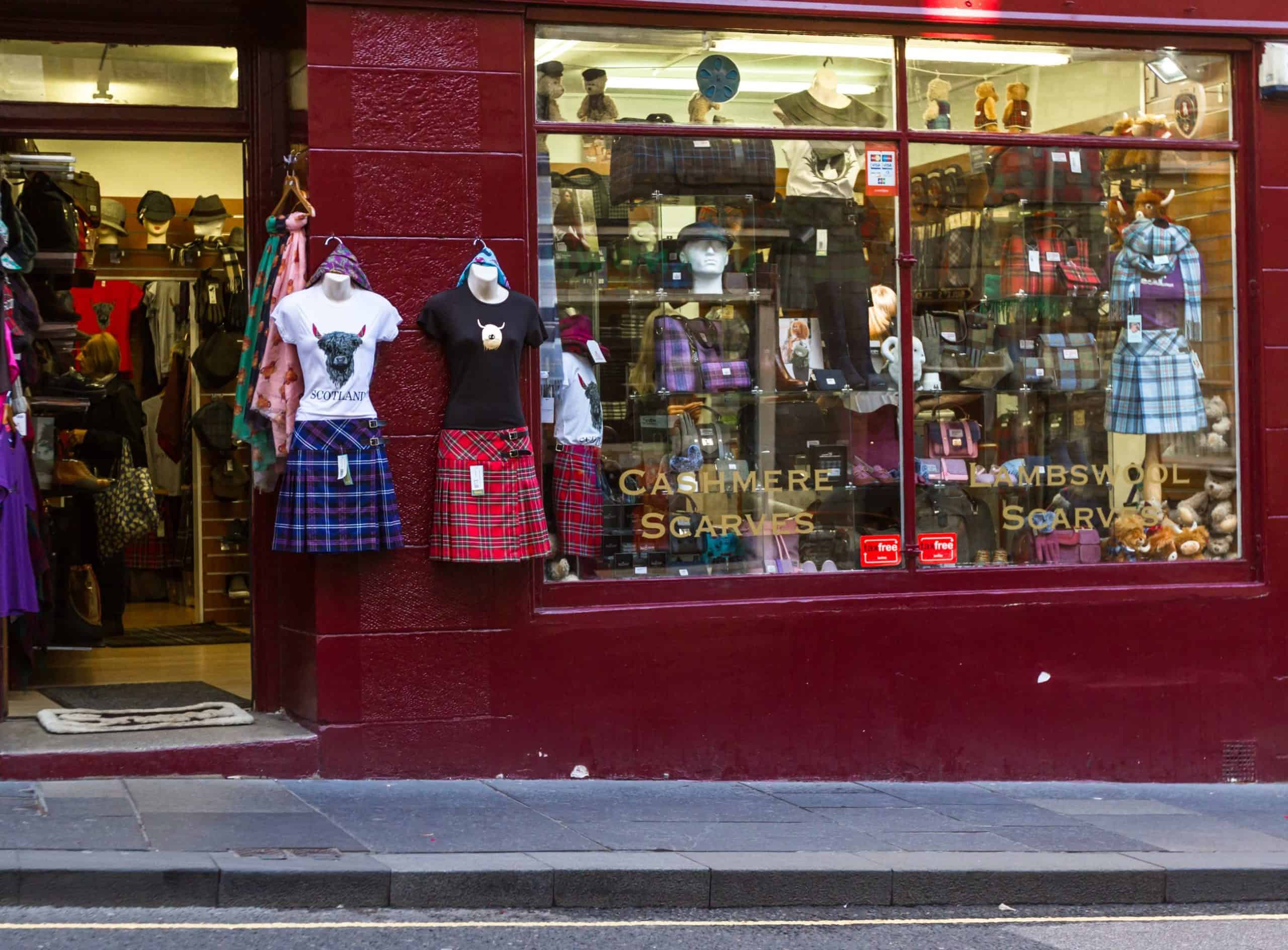 A retail storefront displaying Scottish tartan skirts, wool scarves, and accessories inside a colourful shop, celebrating Scottish heritage and style.