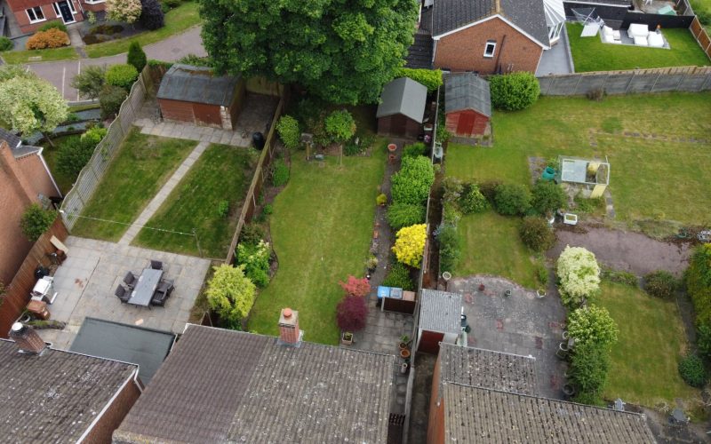 The residential backyards with green lawns, sheds, and patio furniture in a suburban neighborhood.