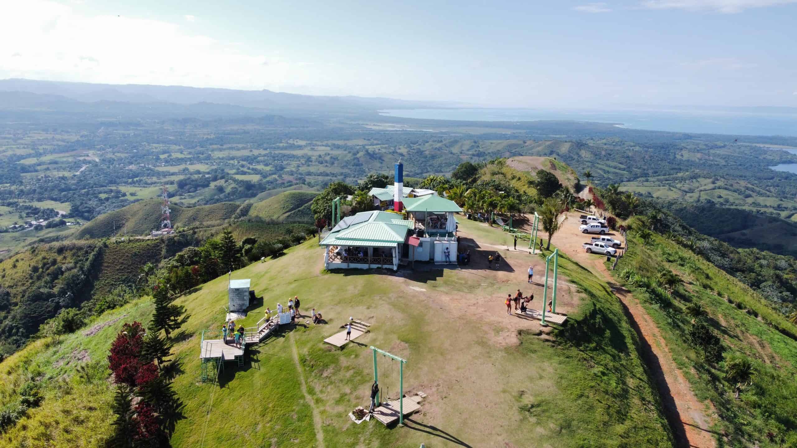 Punta Cana Aerial view of mountain top with a small building and swings, overlooking lush green hills and valle.