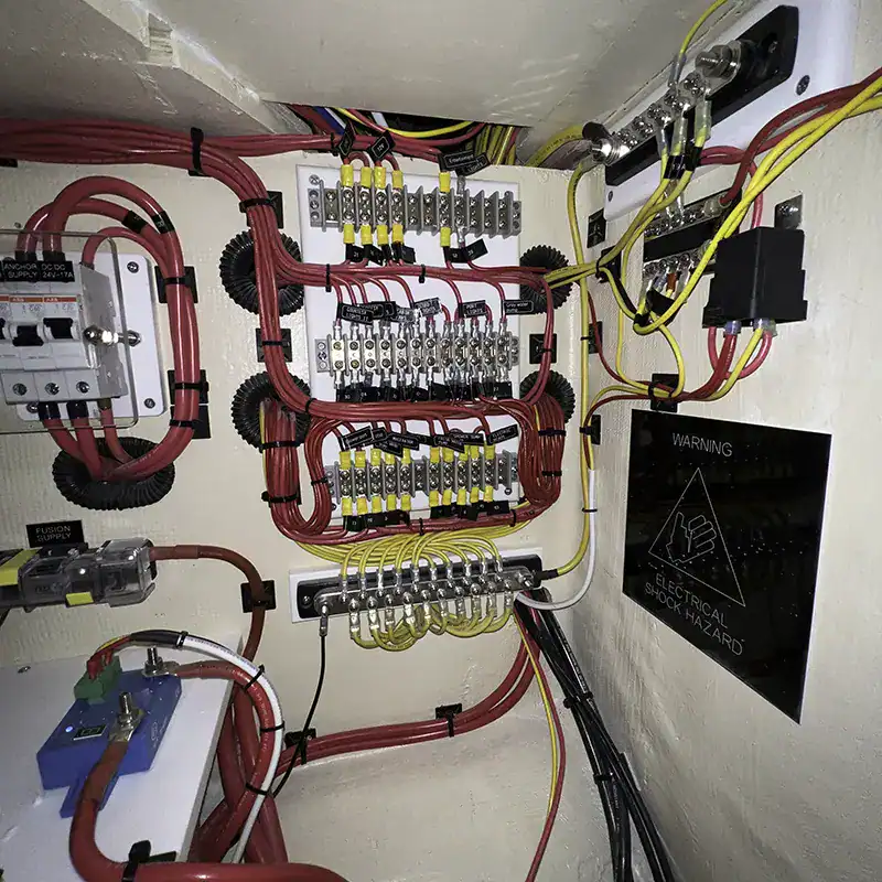 High-voltage electrical control panel with colorful wiring, circuit breakers, and safety warning sign in yacht electrical system.