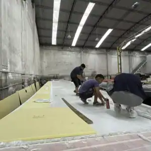 Lightweight yellow foam core panels being assembled for catamaran hull construction at a manufacturing facility. Workers are installing and securing the foam within the boat structure.