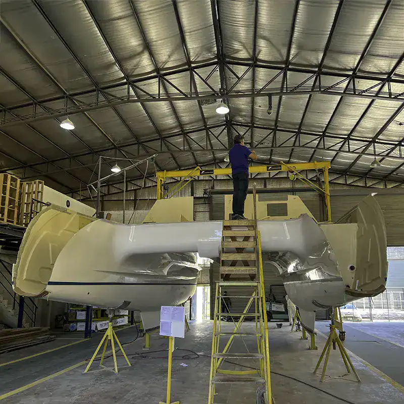 Antores catamaran construction in progress inside a large industrial warehouse with a worker inspecting the vessel's upper section.