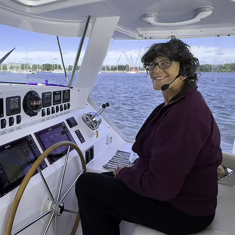 Boat captain on luxury Antares catamaran with navigation instruments and scenic waterway background.