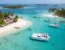 An elegant white catamaran floating in clear, calm Caribbean waters near a tropical island with palm trees and thatched-roof huts, perfect for serious cruisers seeking adventure and relaxation.