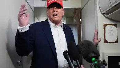 Donald Trump wearing a "Make America Great Again" hat, speaking to reporters.