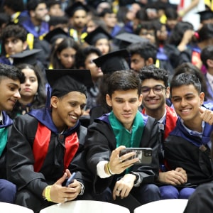 Graduates in caps and gowns smiling and taking a selfie together at a ceremony.