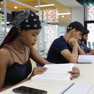 Three people studying at a table in a library, focused on books and notes, with a phone nearby.