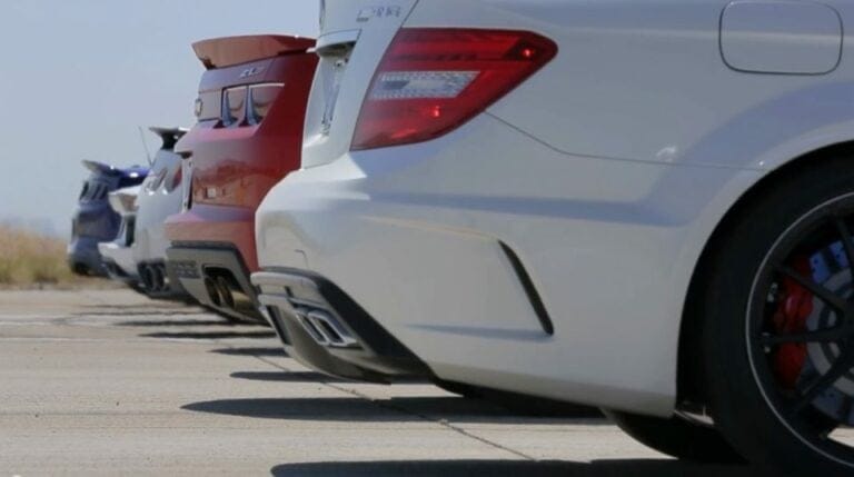 Une rangée de voitures de sport vues du côté arrière droit, garées sur une surface pavée, semble prête pour un comparateur de prix, présentant différentes couleurs et des pare-chocs sportifs sous un ciel clair.