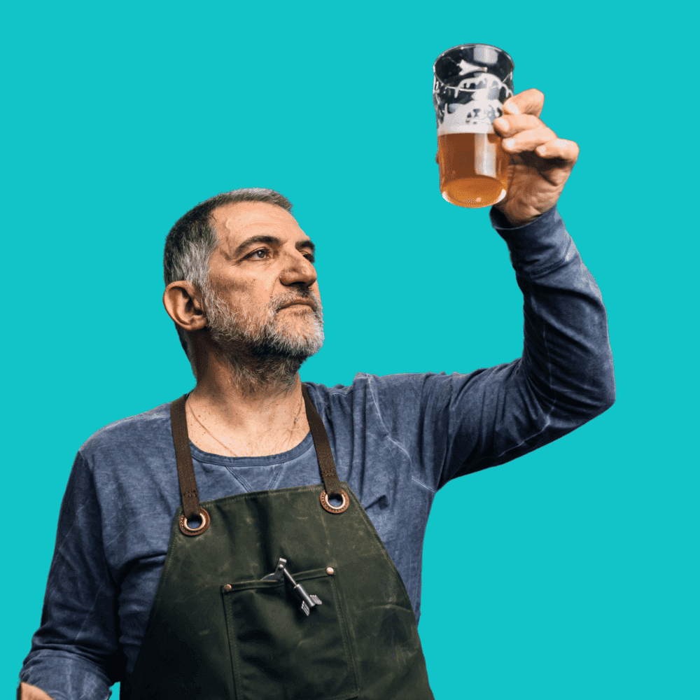 Un homme barbu, vêtu d'un tablier vert et d'une chemise bleue, inspecte une pinte de liquide ambré, sous le regard attentif du propriétaire d'une brasserie artisanale qui s'assure de la qualité de ses produits. L'arrière-plan cyan uni souligne son expression pensive.