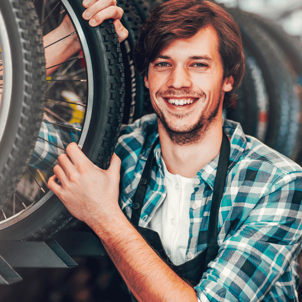 Homme souriant avec pneu de vélo en atelier.