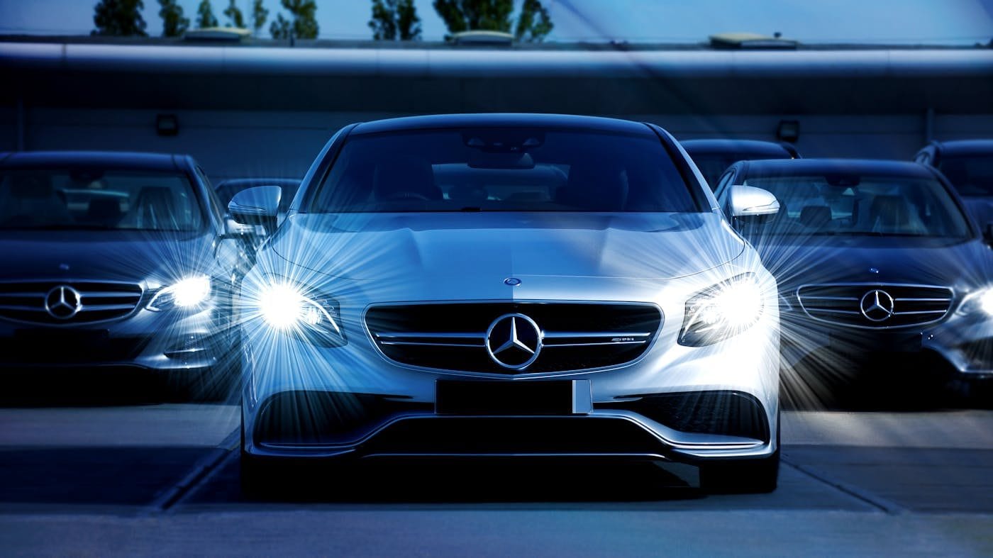 Voiture Mercedes-Benz blanche avec phares allumés, vue frontale.