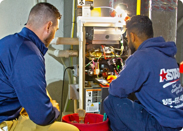 Two technicians from Astar expertly work on a furnace, carefully inspecting and utilizing a precision tool while surrounded by an array of repair equipment.