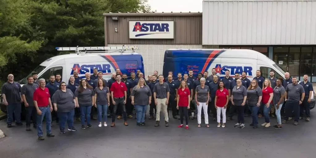A group of people wearing branded shirts stands proudly in front of two company vans, each adorned with the logo, while a building behind them displays the same emblem, embodying the spirit of our "About Us" story.