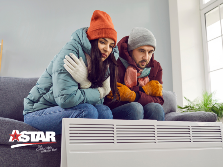 A man and woman in winter clothing sit on a couch, huddled and looking cold in front of a large heater, reassuringly backed by ASTAR's logo, promising warmth with a reliable maintenance plan.