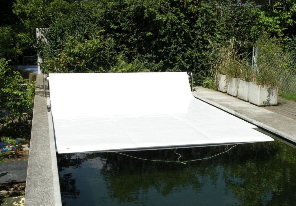 Protezione solare per piscina, telo copri piscina bianco, copertura estiva per piscina interrata, wellness outdoor in ambiente verde, giardino con piscina e copertura mobile.