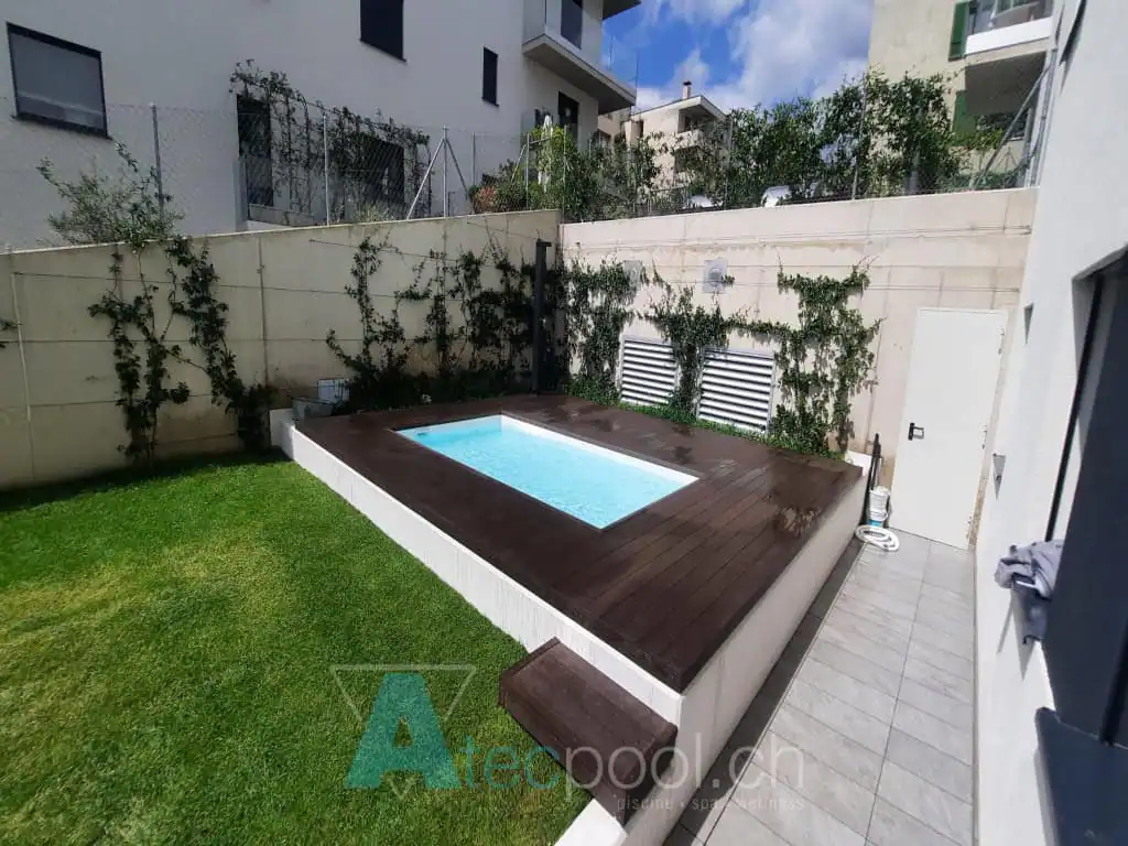 Piccola piscina interrata con bordo in legno in un giardino urbano.