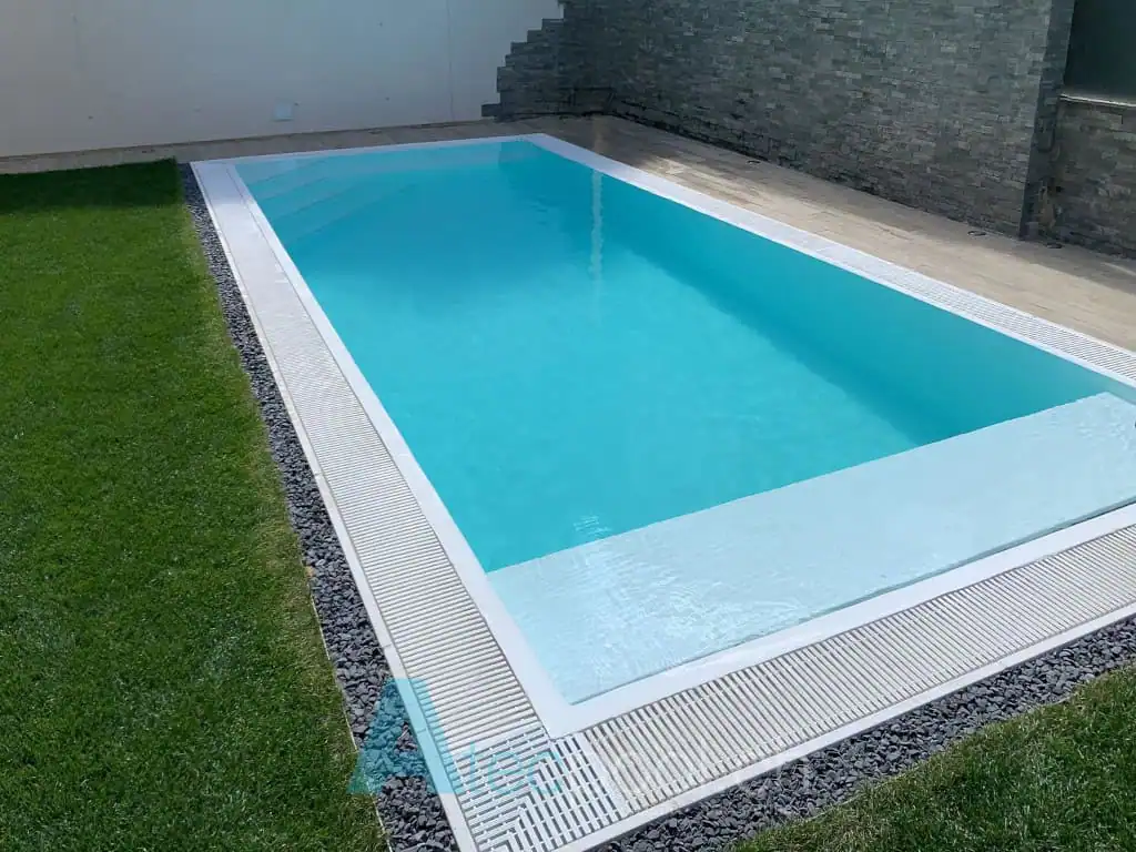Piscina interrata a sfioro con bordo a filo, circondata da prato e pavimentazione in pietra, ideale per relax e nuoto nel giardino.