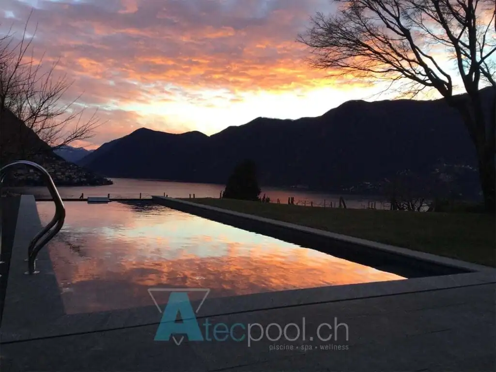 Azzurro piscina interrata con vista sul lago e montagne al tramonto.